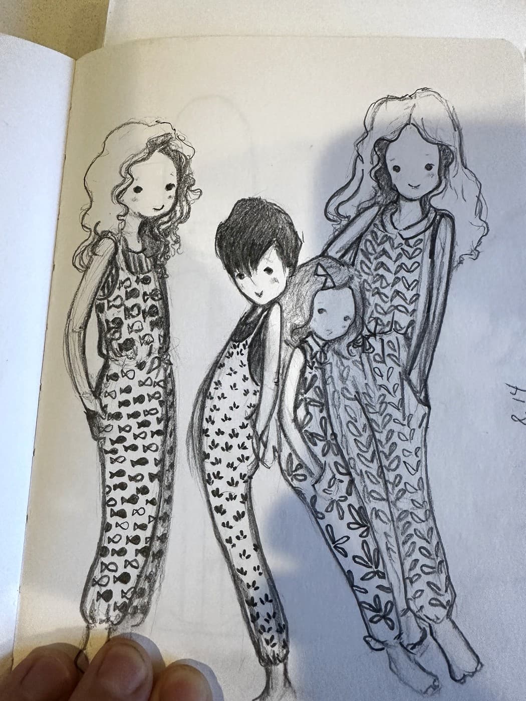 A graphite sketchbook page of four girls with different hair, each in a dress patterned by hand with tiny drawn shapes. Every face is two solid dots and a small mouth.