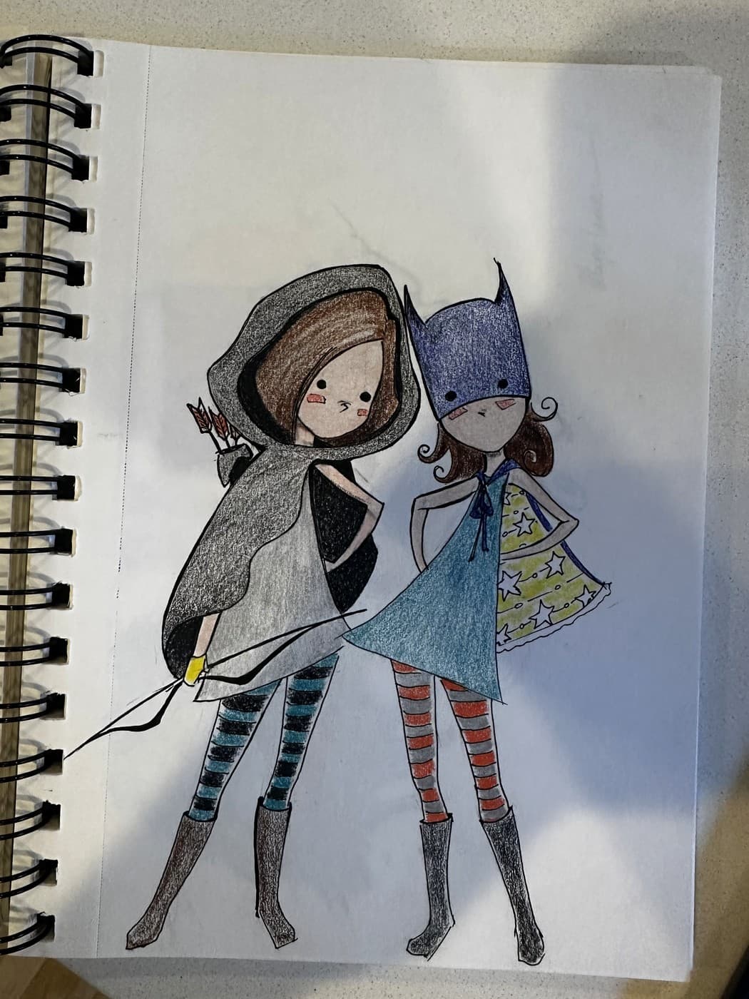 Alyx's finished drawing of the two characters in ink and coloured pencil: Archer in a grey hood with a bow and arrows, Super in a blue pointed mask with a star-patterned cape, both in striped socks and boots.